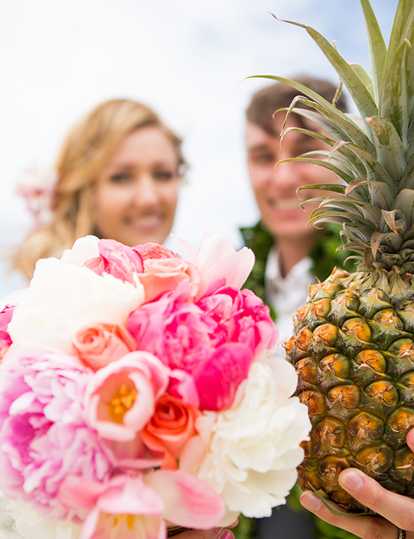Bride holding a pink peony bouquet as the groom holds a pineapple after their wedding