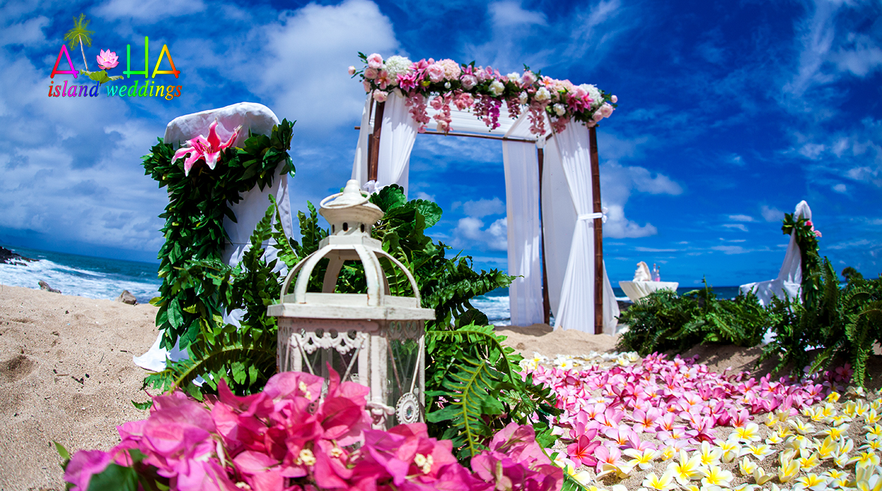 White bamboo arch with lanterns and pink flowers on the sand