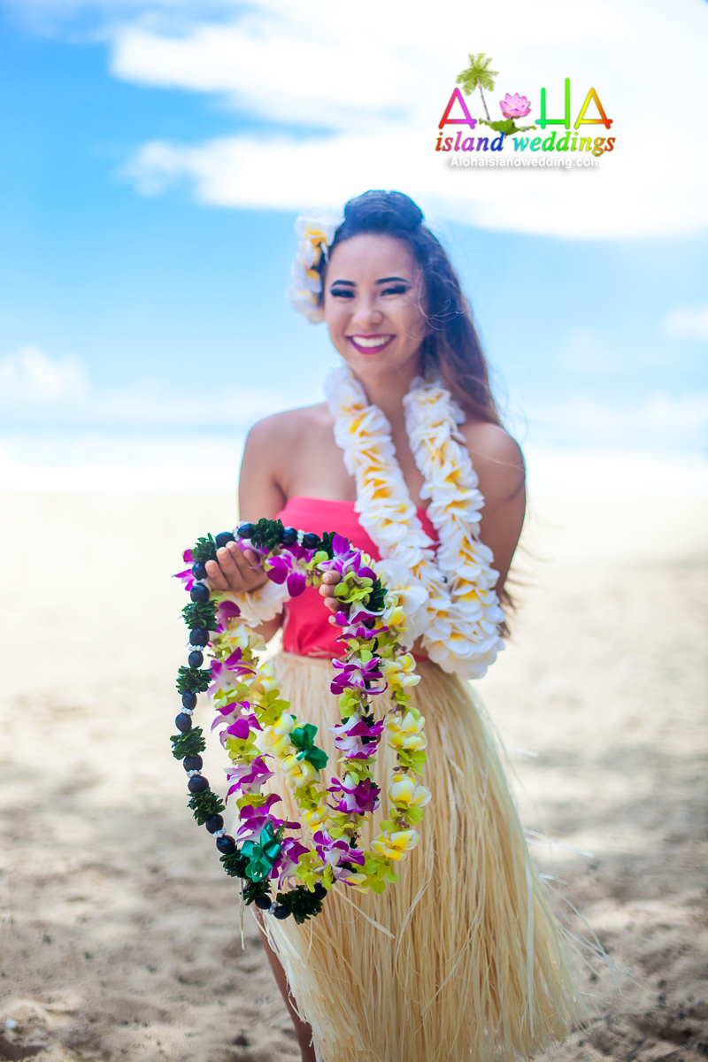 Smiling hula dancer in a grass skirt holding colorful flower leis on the beach
