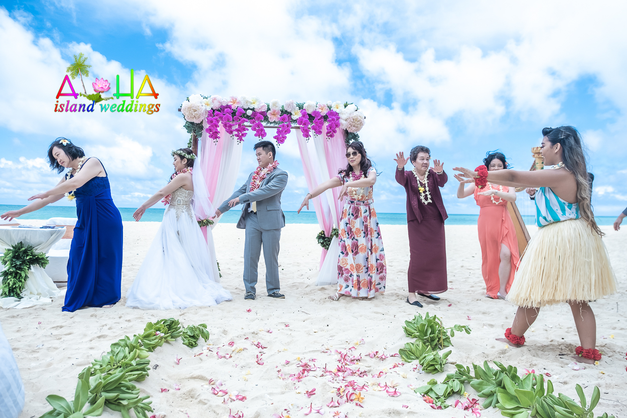 Family and guests at a wedding ceremony in Hawaii practice their first hula dance on the beach