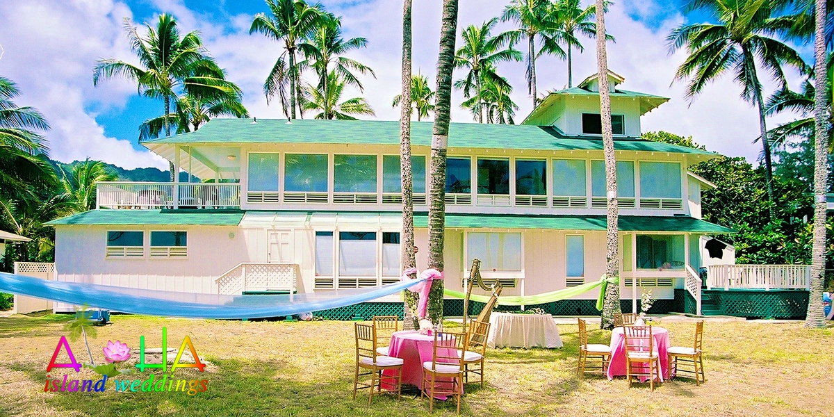 Green and white estate house with a reception set up on the lawn under the palms