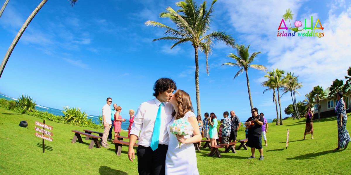 Couple kissing on the lawn as guests mingle under the palm trees