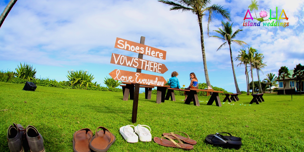 Wooden welcome sign on the lawn with guests' sandals lined up beneath palm trees