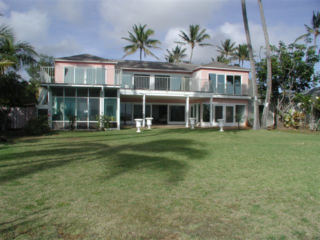 Pink beachfront estate house with a wide green lawn and palm trees