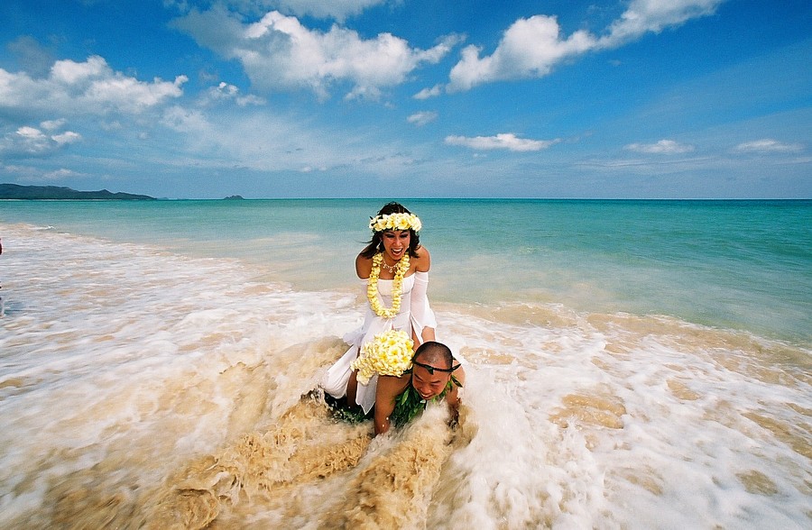 bride rides her husband having fun in the water wearing a yellow plumeria flower lei