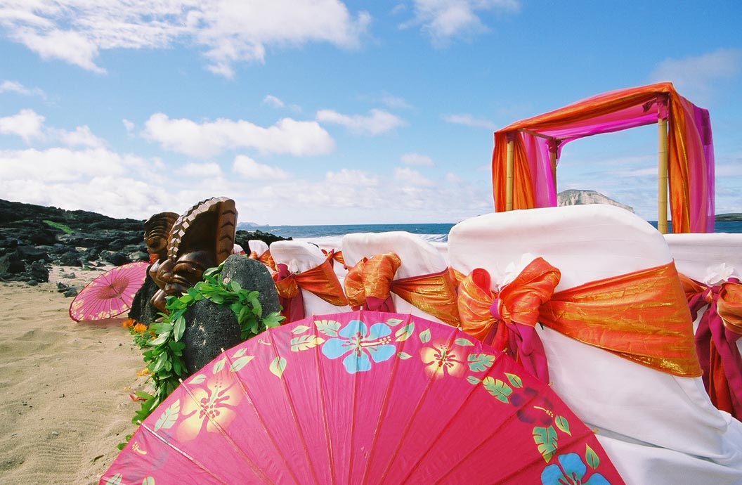 A flowered pink parasol beside the chairs, a tiki and the arch on the beach