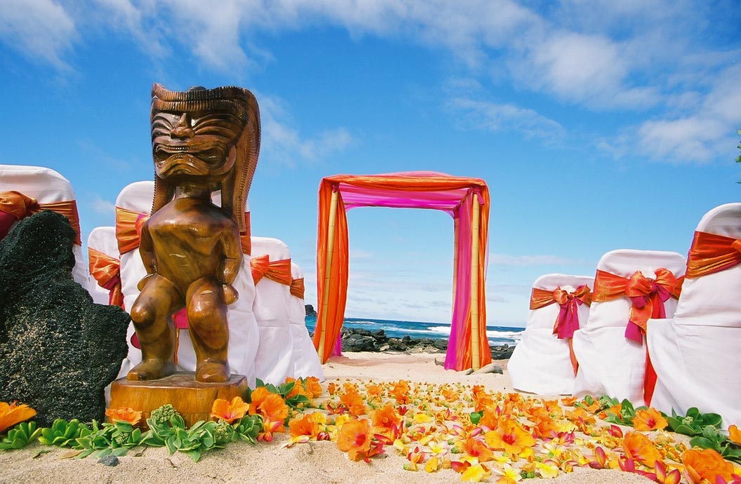 A tall carved tiki at the start of an orange plumeria aisle leading to the fuchsia arch