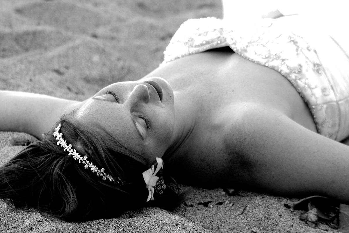 Black and white photo of the bride lying on the sand with her eyes closed