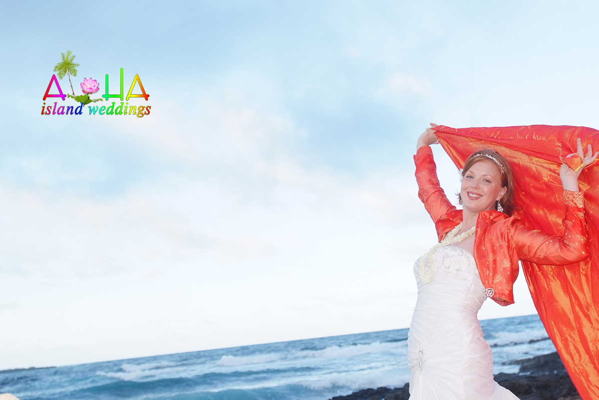 Smiling bride holding orange chiffon from the arch up in the wind by the ocean
