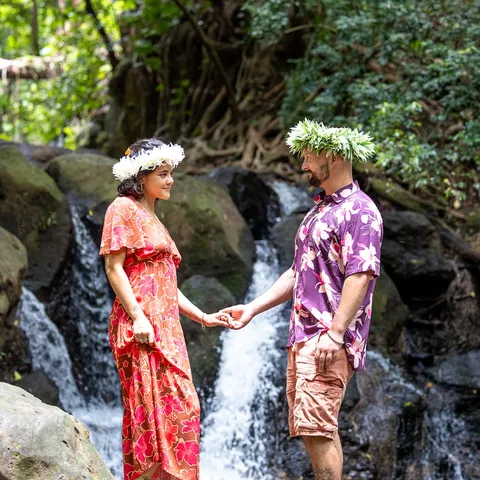 Samara and her fiancé in flower crowns holding hands by a waterfall