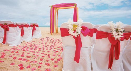 white ginger lei is wrapped over the white wedding chair with a fuchsia sash